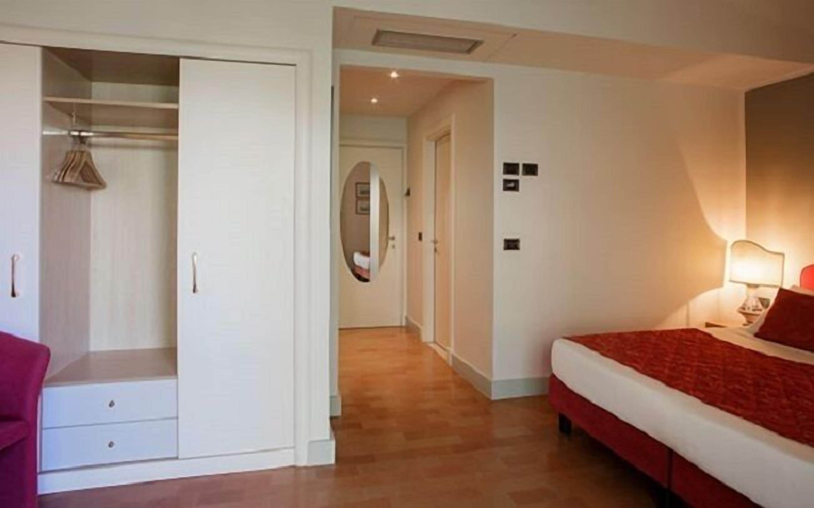 Un dormitorio con cama, armario, espejo y lámpara de noche.