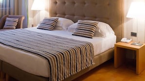 A hotel room with a large bed, striped bedding, a tufted headboard, two bedside lamps, and a bedside phone. - Hotel Dei Duchi (Spoleto)