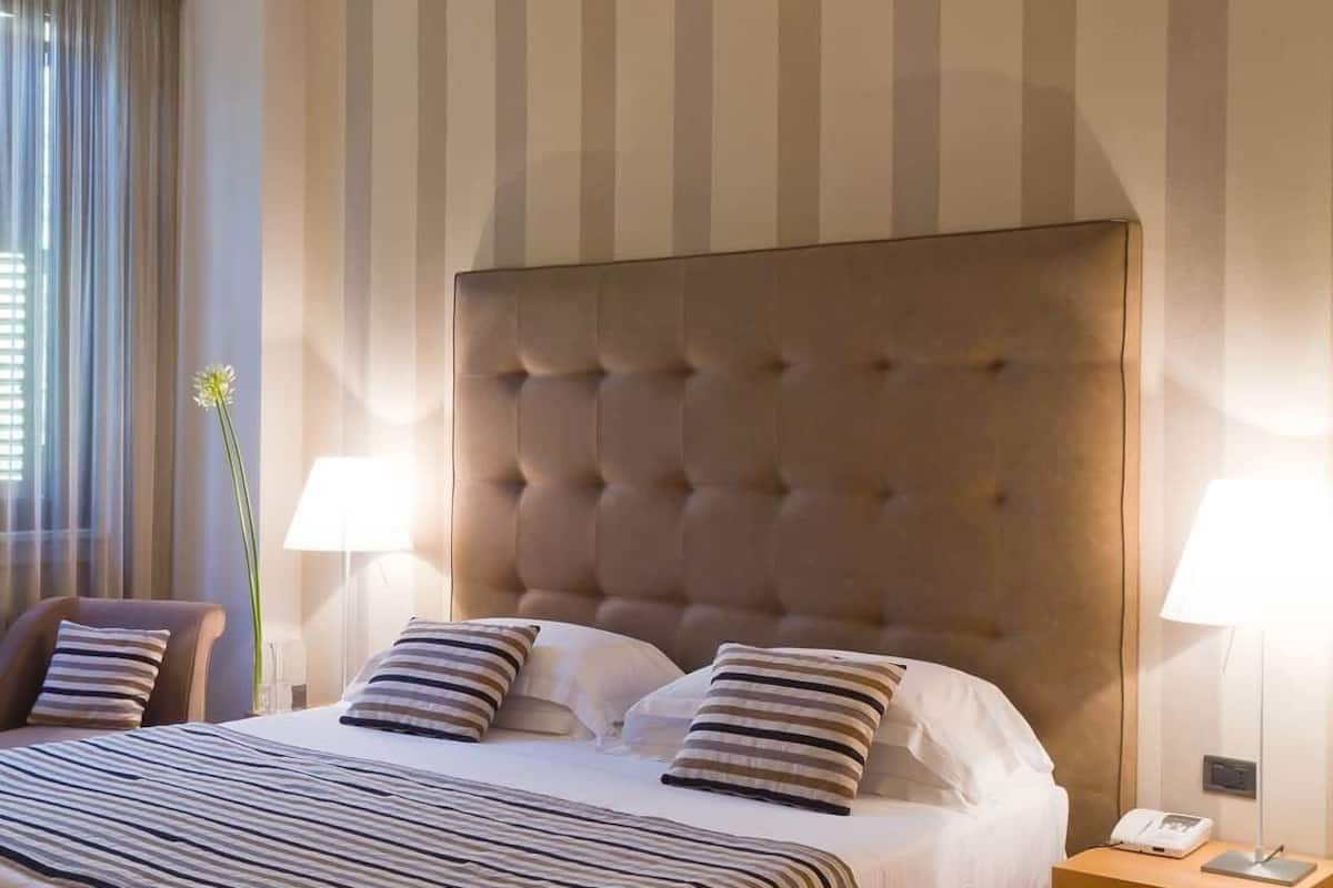 A hotel room with a large bed, striped bedding, a tufted headboard, two bedside lamps, and a bedside phone.