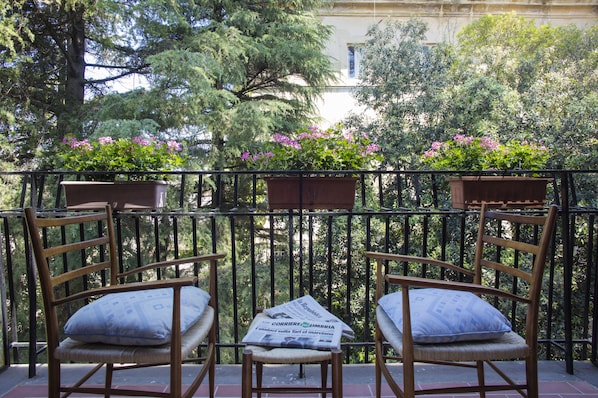 A balcony with two wicker chairs and a small table, surrounded by a black metal railing.