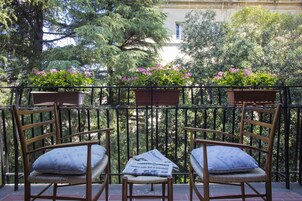 A balcony with two wicker chairs and a small table, surrounded by a black metal railing.
