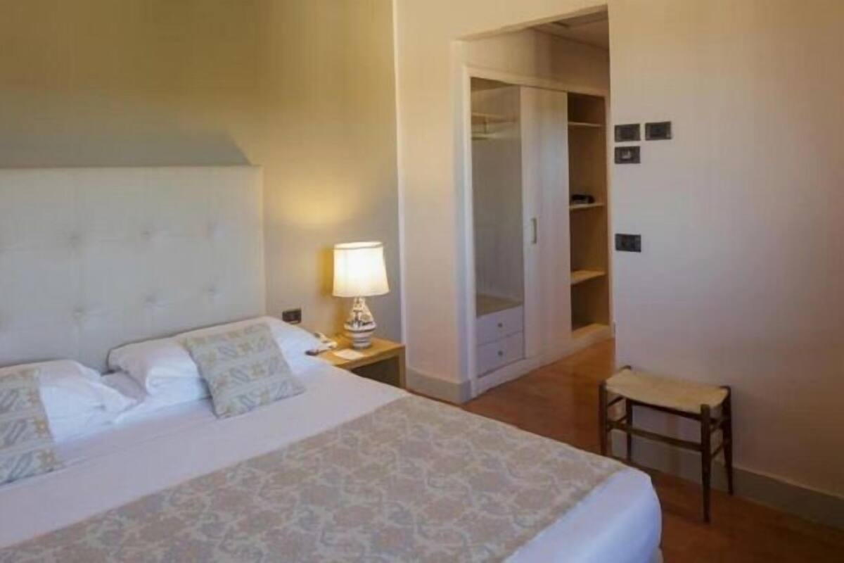 A hotel room with a bed, a nightstand, a lamp, a chair, and a wardrobe.