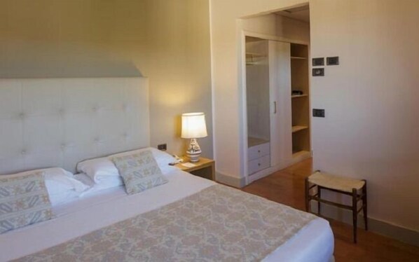 Una habitación de hotel con cama, mesita de noche, lámpara, silla y armario.