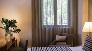 Habitación de hotel con cama, escritorio, silla, lámpara y ventana con cortinas.