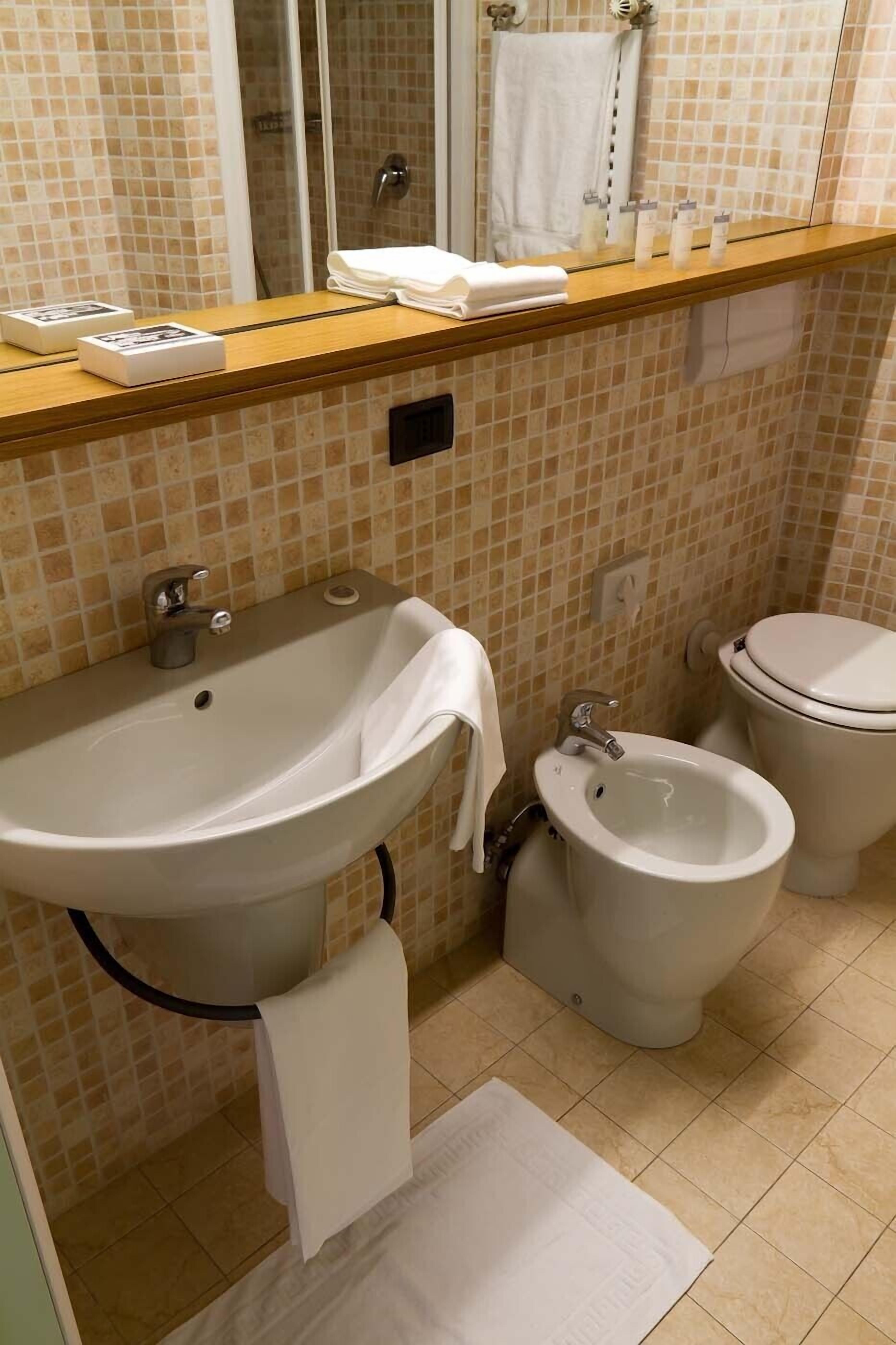 Un baño con lavamanos, bidé y retrete, con azulejos color crema y blanco.