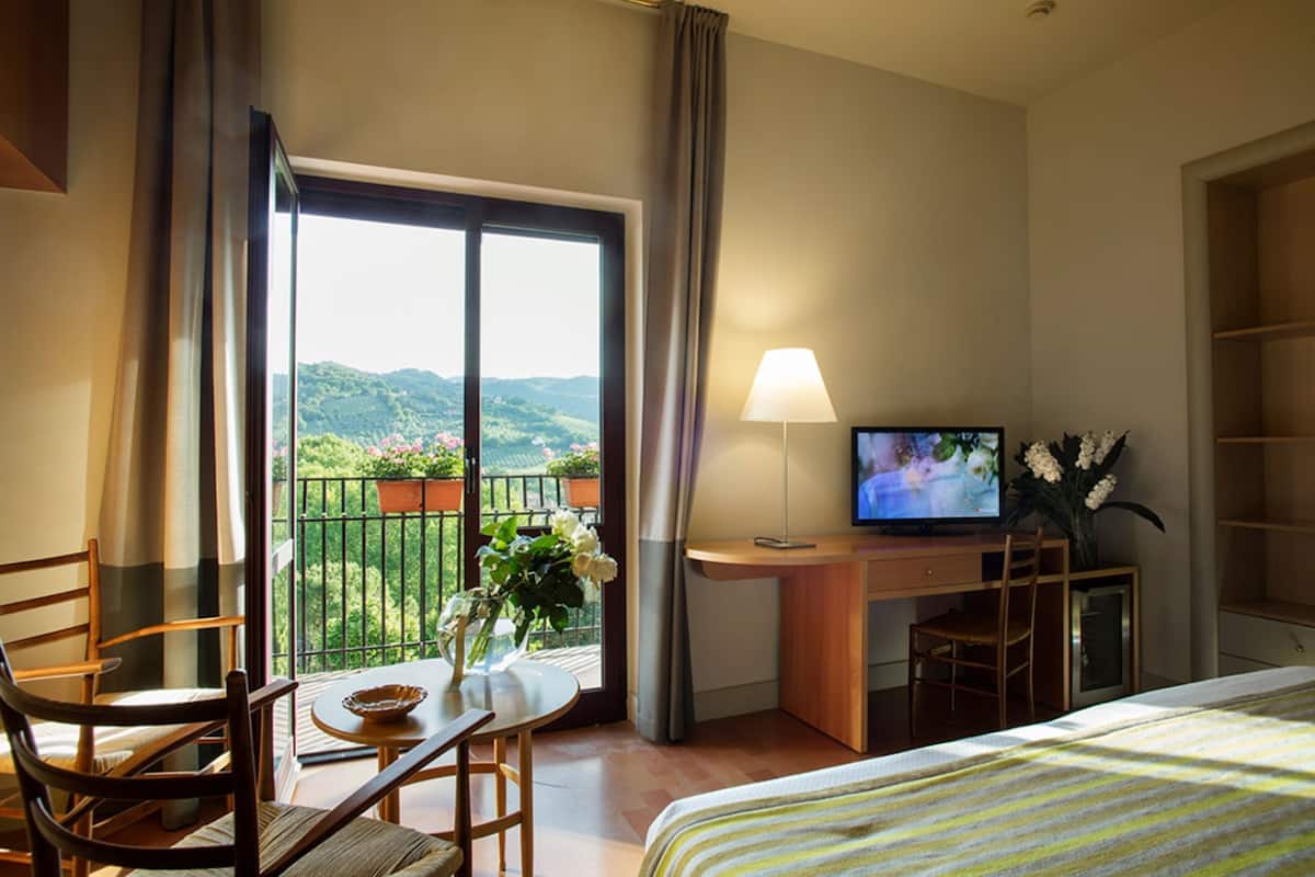 A hotel room with a balcony, a desk with a television, a bed, and a dining area with chairs and a table.