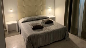 Una cama bien hecha con una colcha estampada y dos almohadas, flanqueada por mesitas de noche blancas con lámparas de pared.