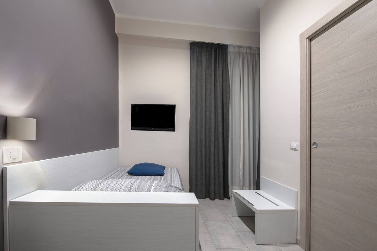 A modern bedroom with a bed, a bench, a TV mounted on the wall, and a door.