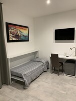 A compact room with a bed, a desk, a chair, a TV, and a small cabinet.