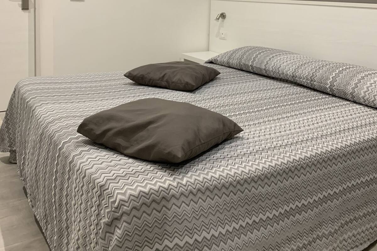 A bedroom with a bed, two pillows, a white nightstand, and a door.