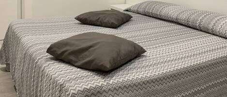A bedroom with a bed, two pillows, a white nightstand, and a door.