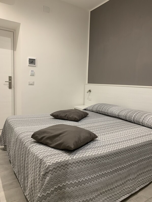 Une chambre à coucher avec un lit, deux oreillers, une table de chevet blanche et une porte.