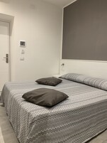 Een slaapkamer met een bed, twee kussens, een witte nachtkastje en een deur.