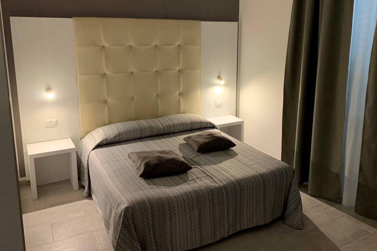 A neatly made bed with a patterned bedspread and two pillows, flanked by white nightstands with wall-mounted lights.