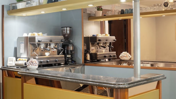 Una cocina con máquinas de espresso, cafetera y un tazón de sobres de azúcar.