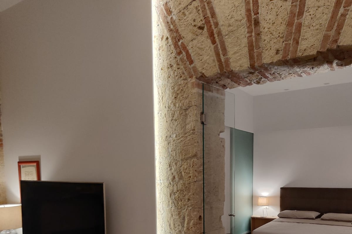 A modern bedroom with a large bed, a television on a wooden stand, and a stone pillar.