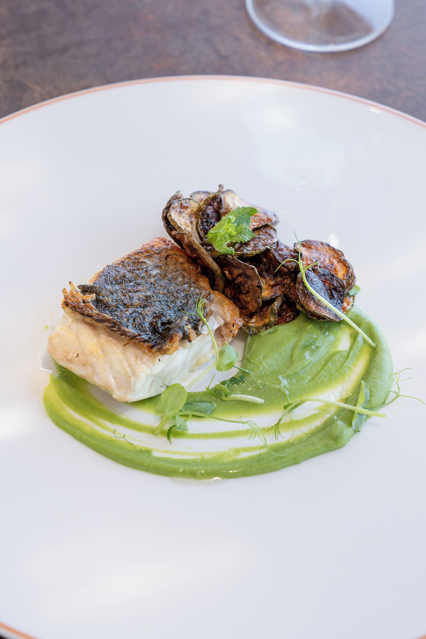 Prato com um pedaço de peixe grelhado, cogumelos e molho verde.