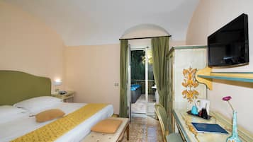 A hotel room with a bed, a desk with a vase, a television, and a view of the outside.