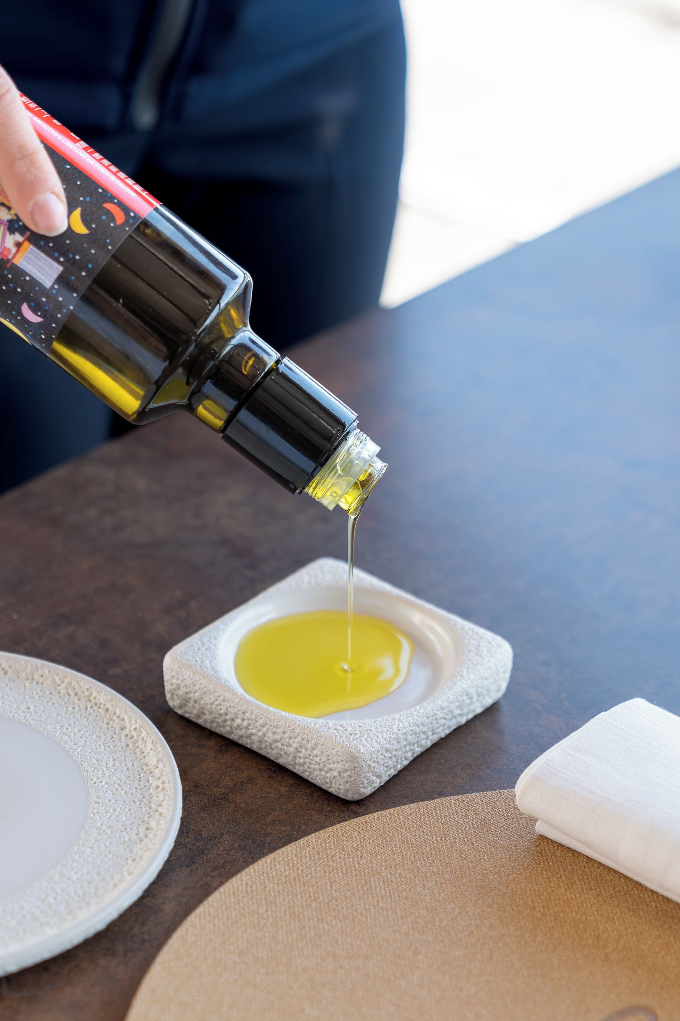 A bottle being poured into a square stone bowl.