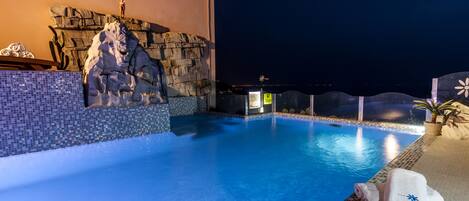 A swimming pool with a rock wall and a statue, a towel, and a plant.