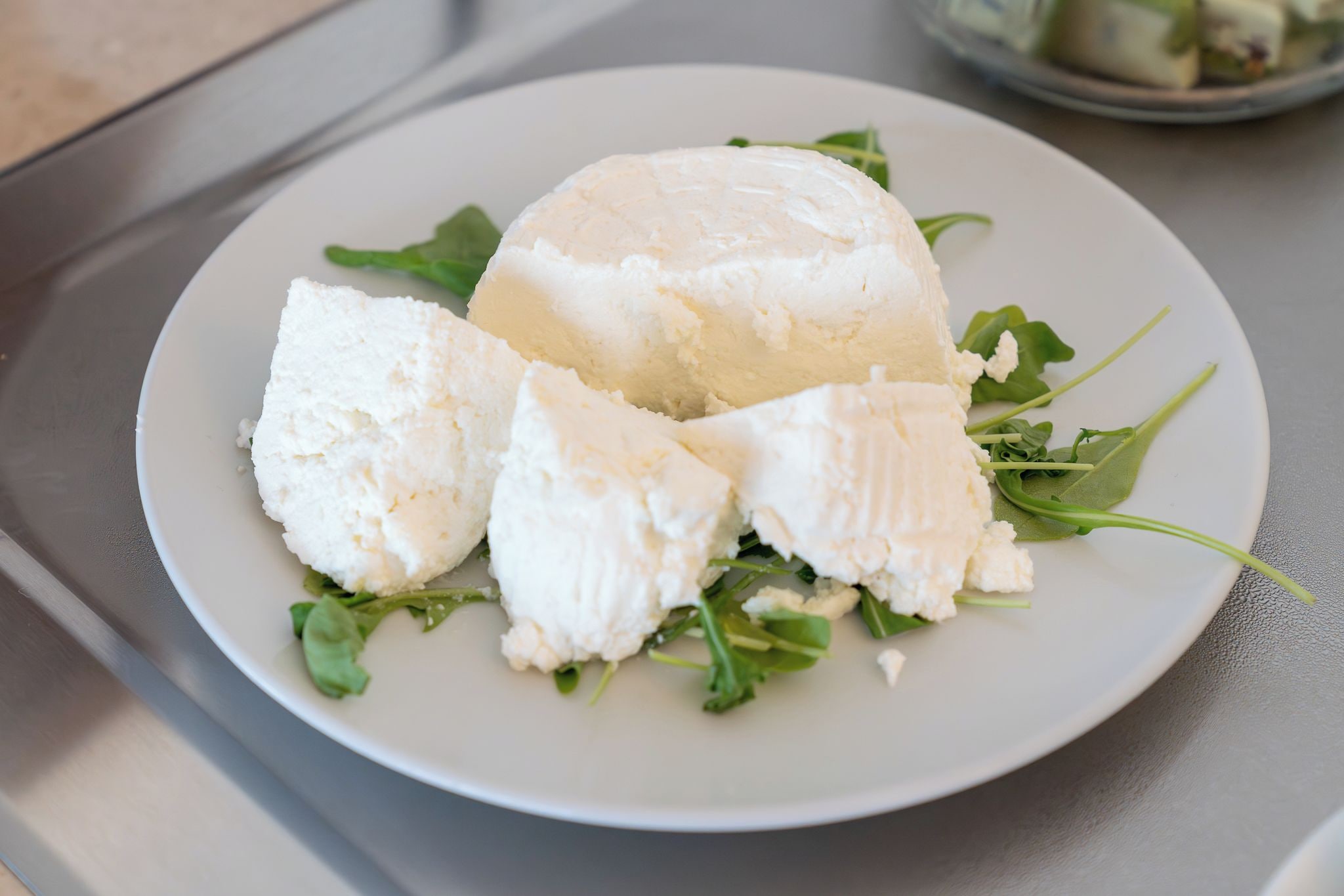 A plate of food with a large white item, possibly cheese, and some green leaves, likely a salad, on a white plate.
