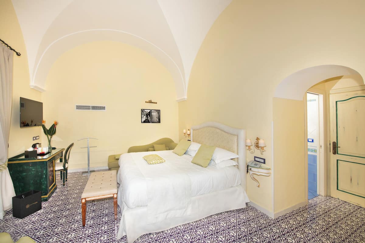 A hotel room with a bed, a desk with a chair, a mirror, and a door.