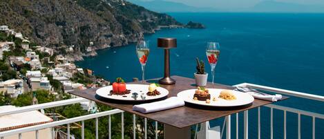 Un balcón con una mesa lista para una comida, con vistas a un paisaje costero.