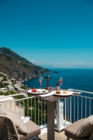 Un balcón con una mesa lista para una comida, con vistas a un paisaje costero.