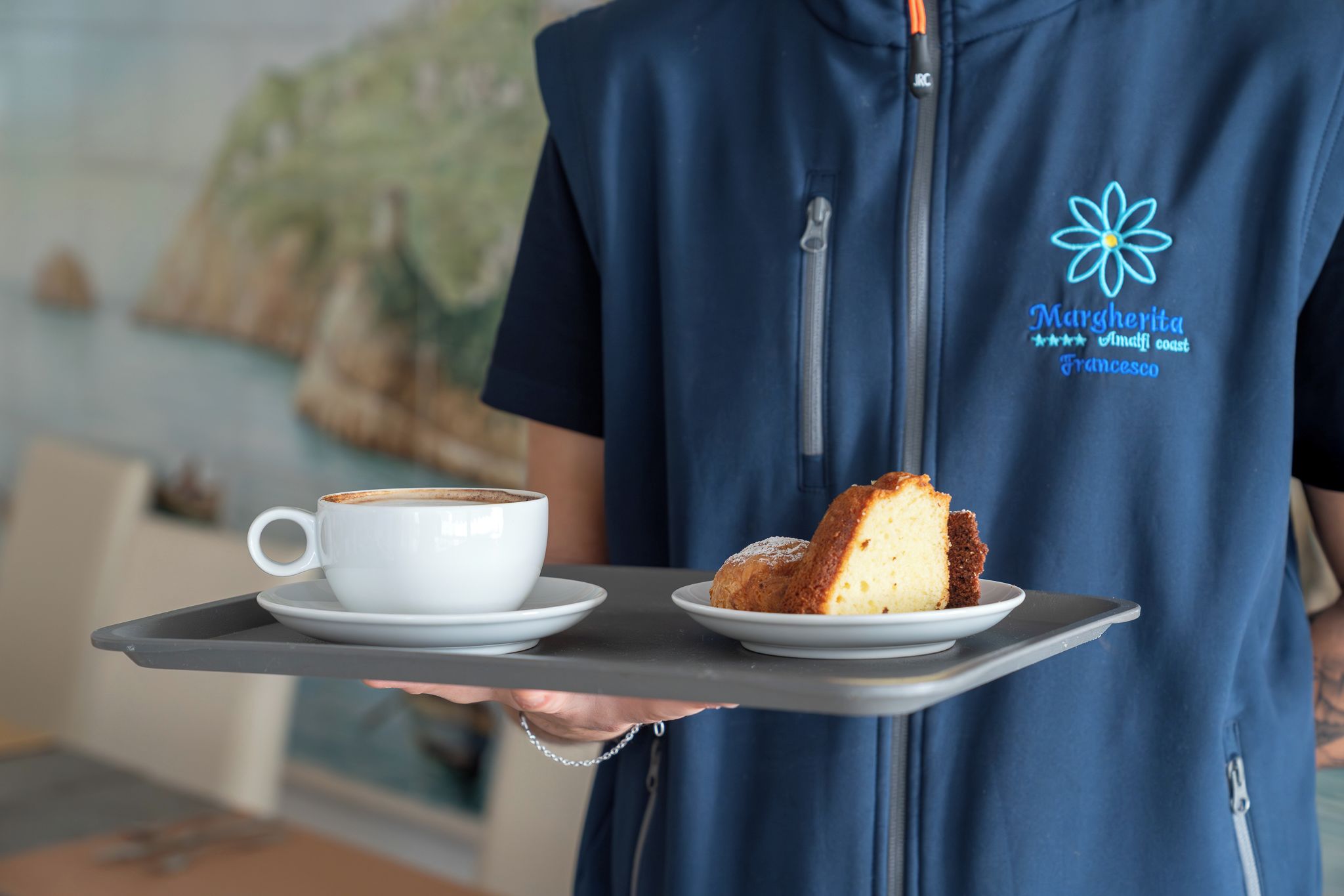Una persona che tiene un vassoio con una tazza bianca e una fetta di torta.