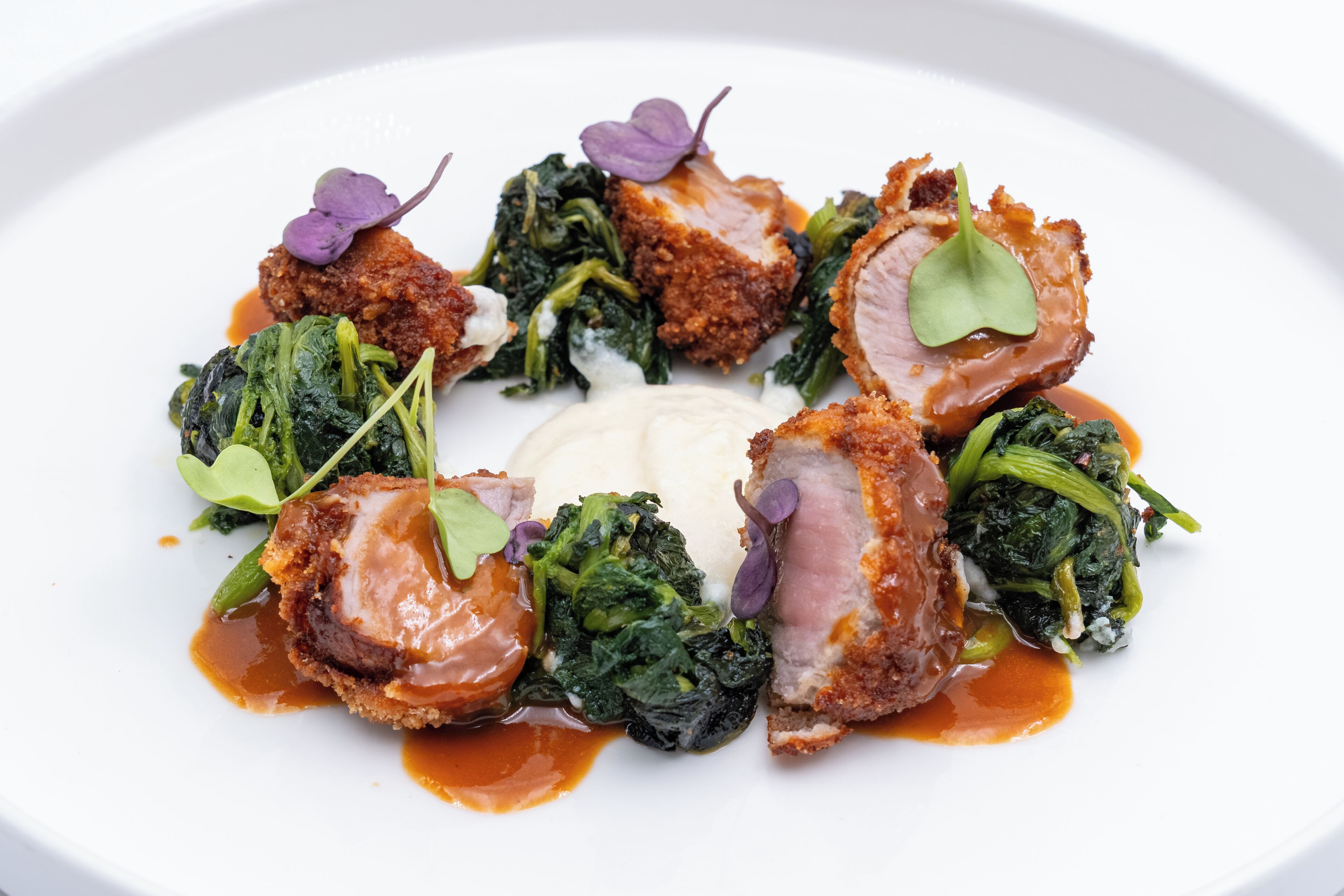 Une assiette blanche contenant un plat de viande, des légumes verts et une cuillerée de crème.