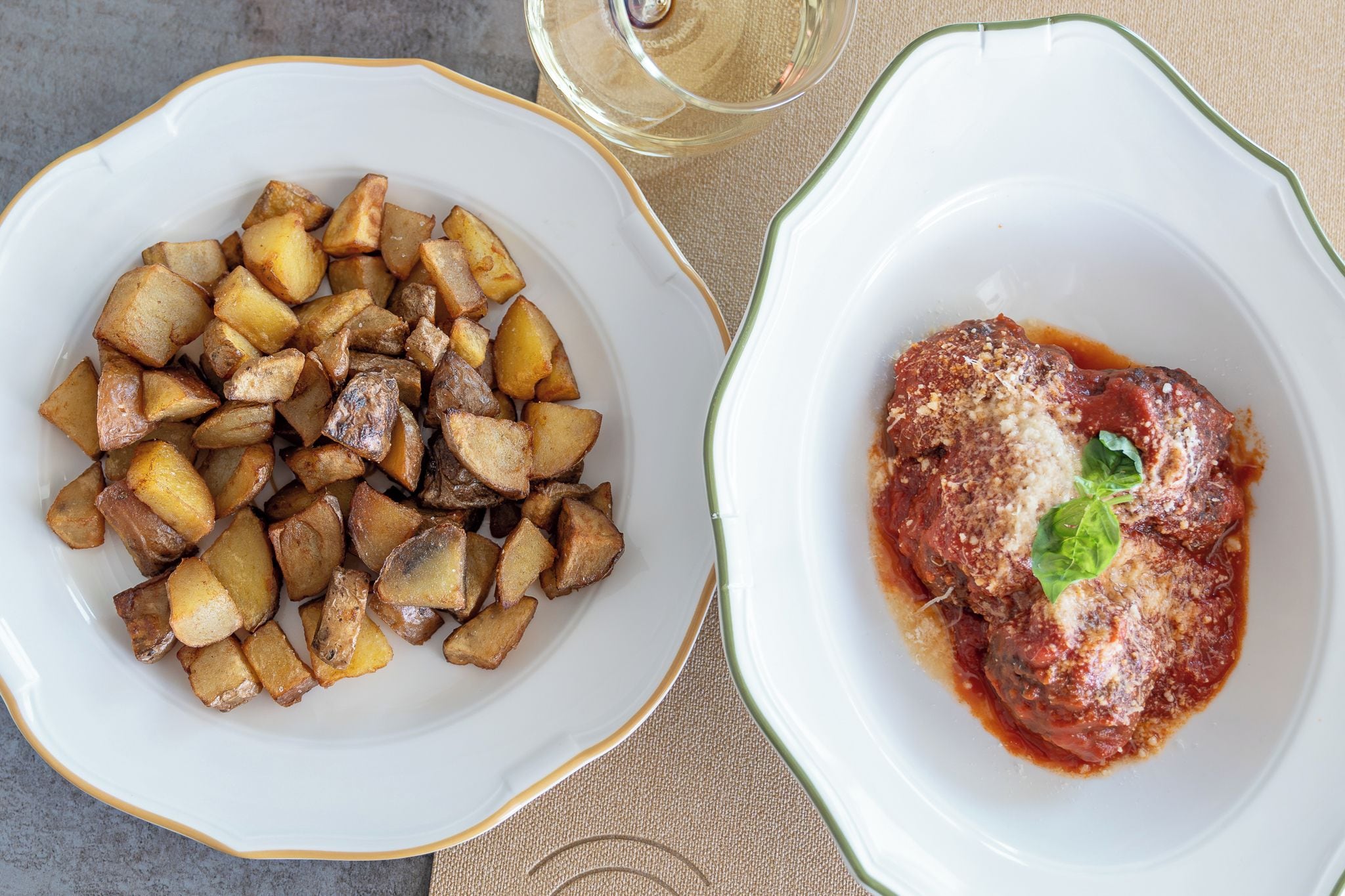 Two plates of food, one with roasted potatoes and the other with a meat dish, on a table.