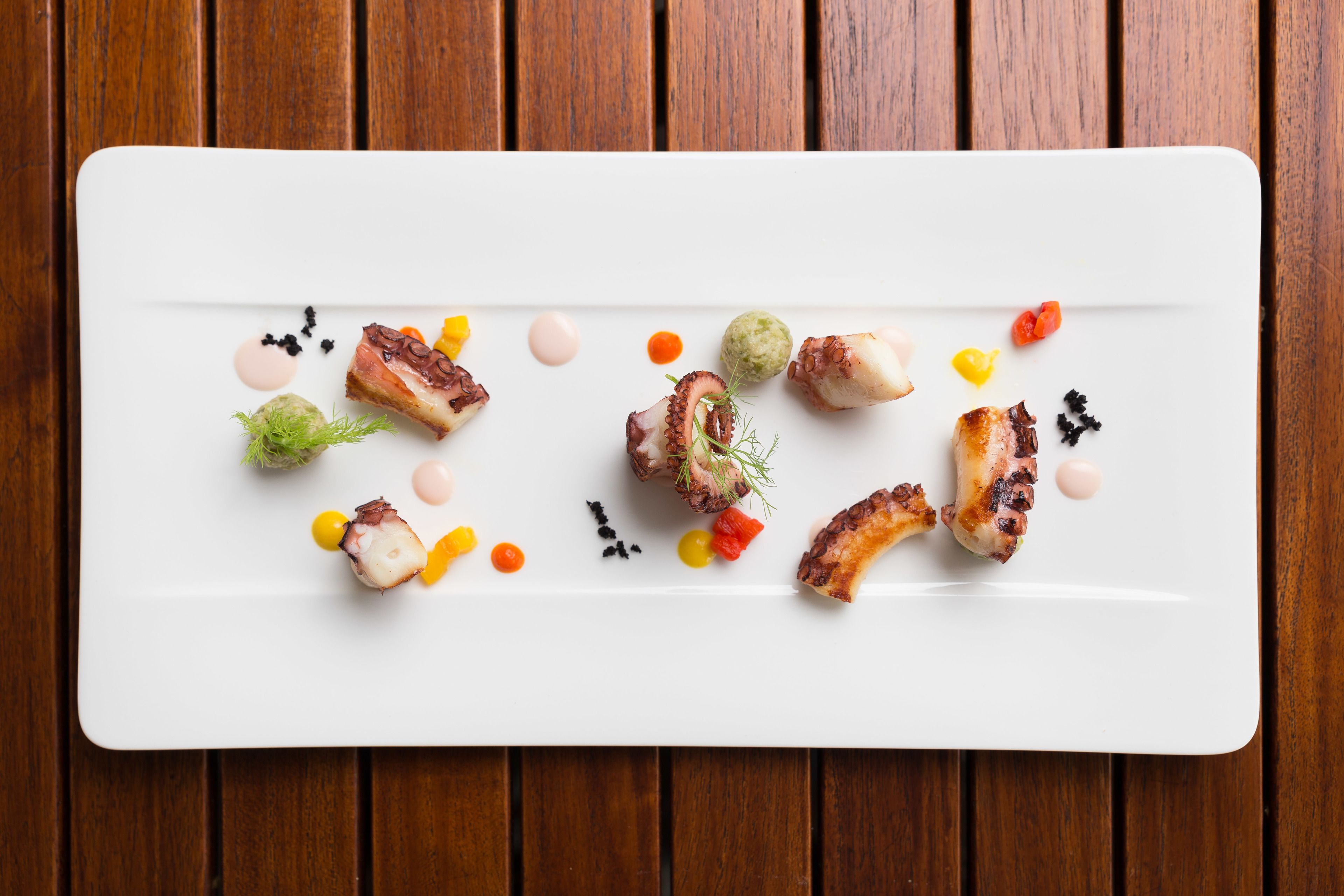 Un plato rectangular blanco con diversos alimentos y adornos sobre una mesa de madera.