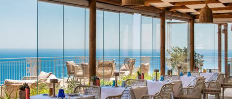 Een restaurant met rieten meubels, witte tafellakens en uitzicht op zee.