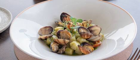 A table with a white plate of mussels, a bowl of butter, a loaf of bread, and a small potted plant.