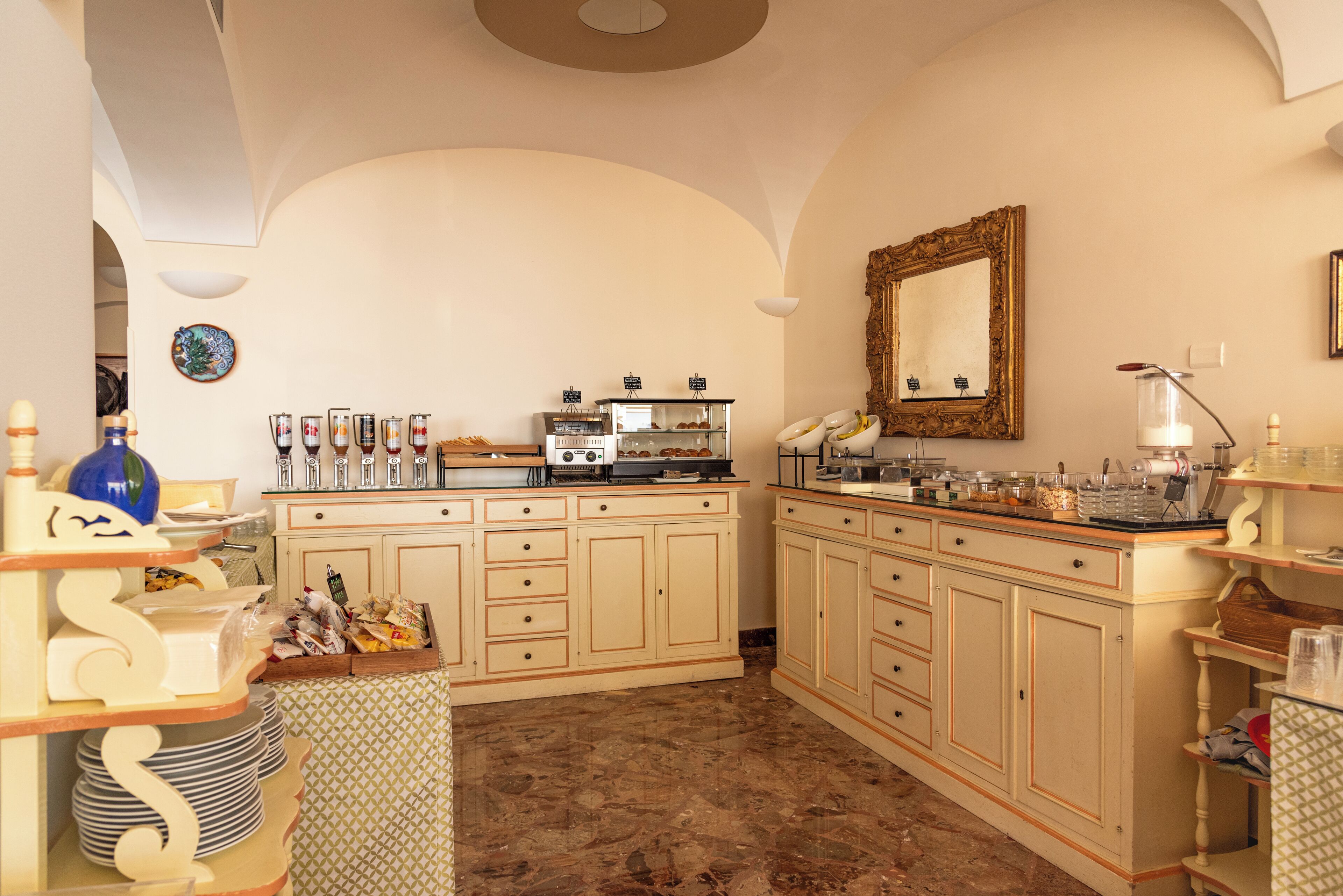 A spacious kitchen with a marble floor, a coffee station, and a large mirror on the wall.