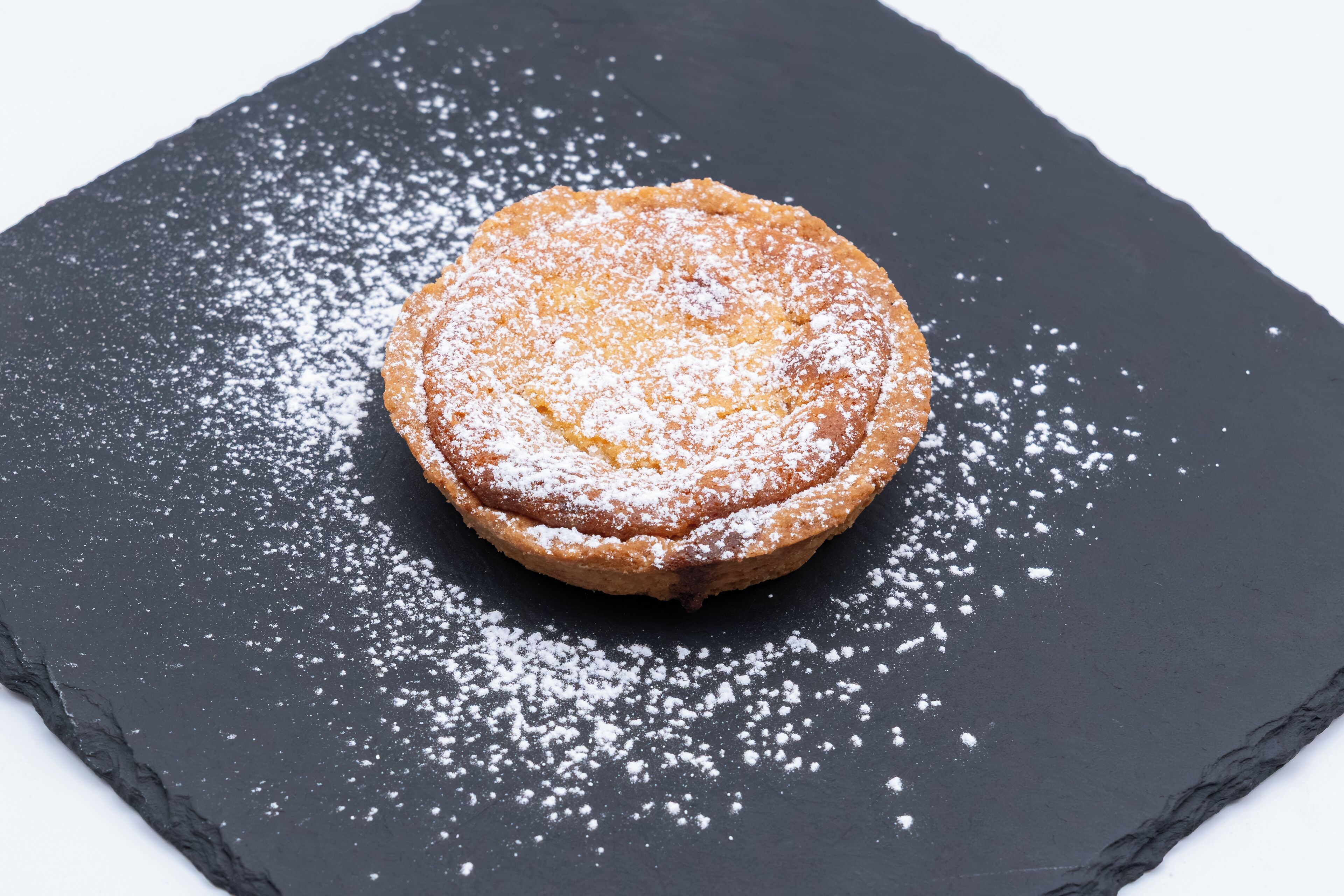 Un pastelito redondo sobre una superficie de pizarra negra cubierta de azúcar glas.