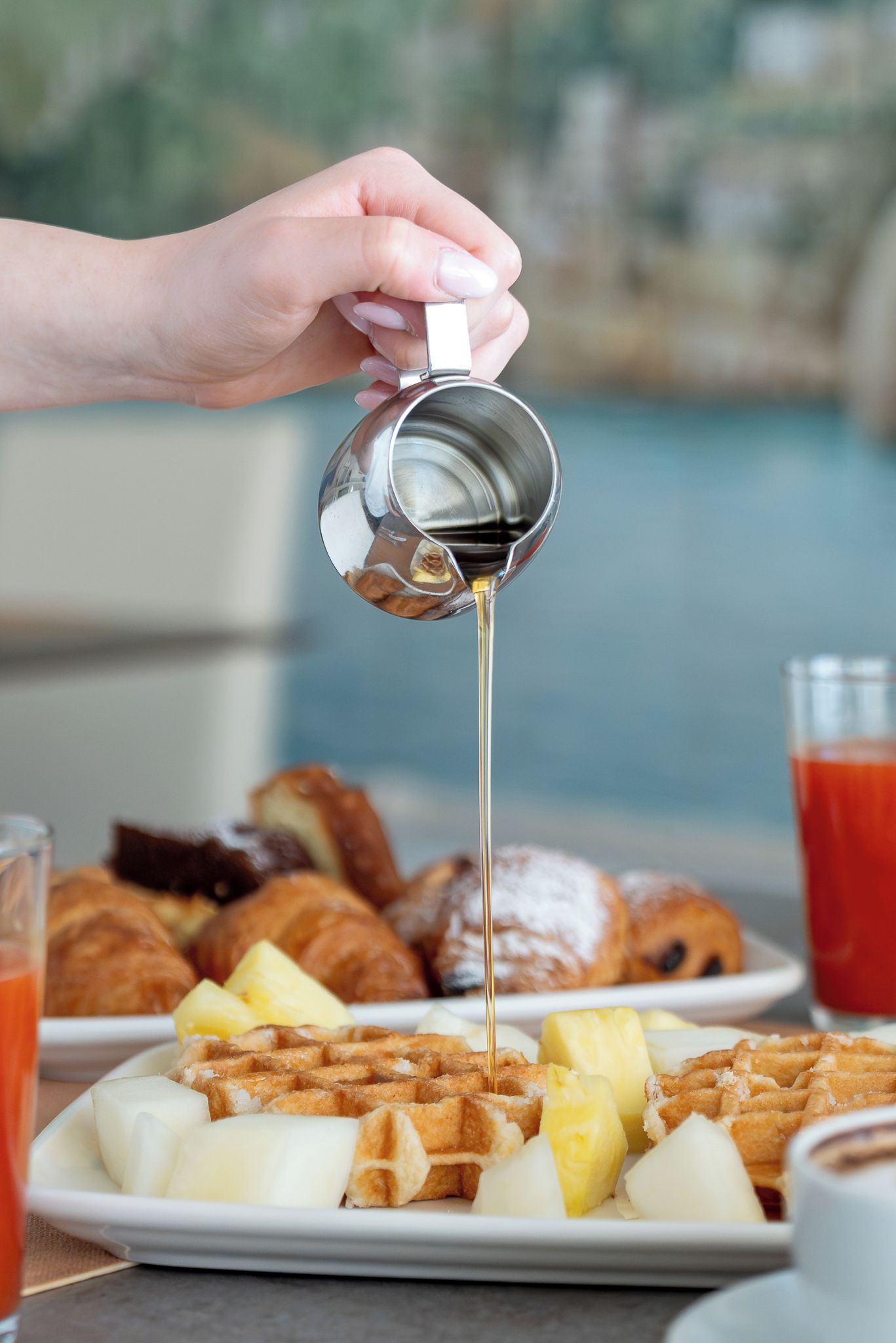 Une main versant du sirop sur des gaufres et des crêpes.