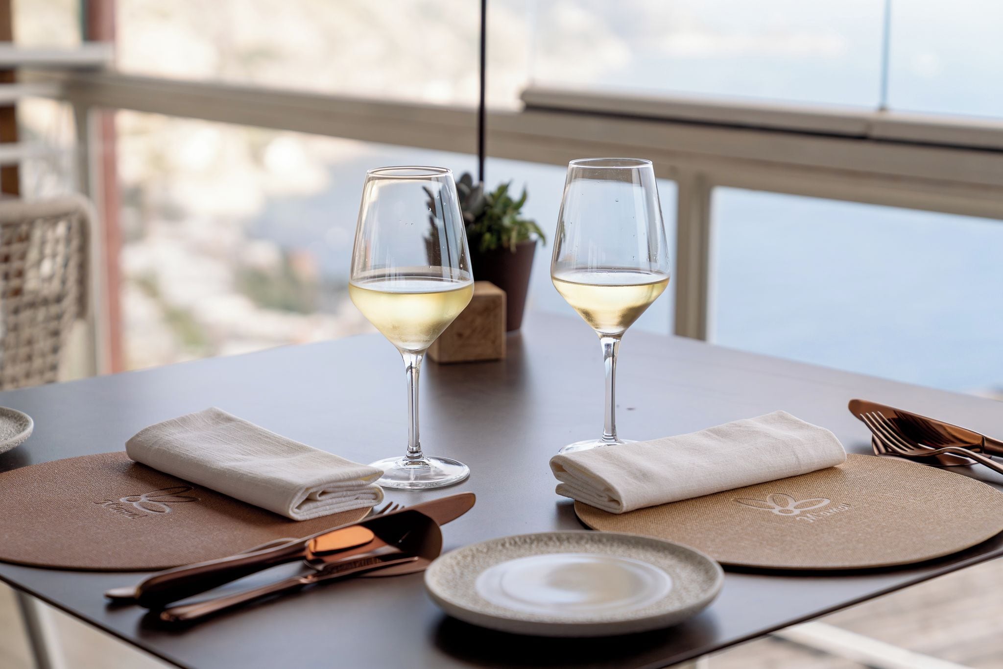 Una mesa dispuesta con dos copas de vino, un plato, cubiertos y una servilleta.