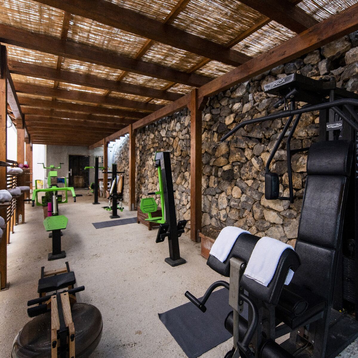 Un gimnasio con diverso equipamiento de ejercicio, incluyendo un banco de pesas, una estructura para sentadillas y un banco con una toalla.