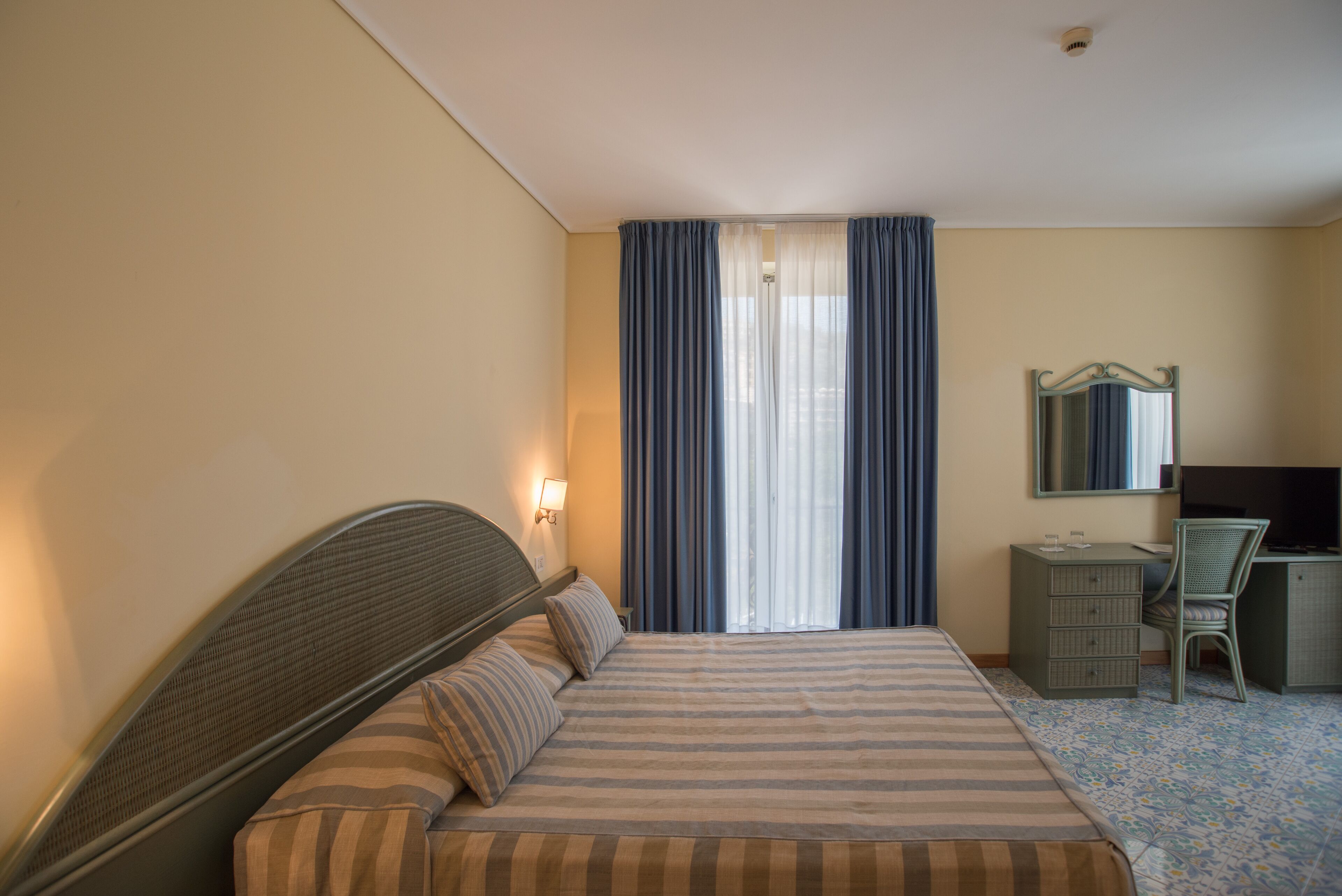 A hotel room with a bed, a desk, a chair, a dresser, and a mirror.