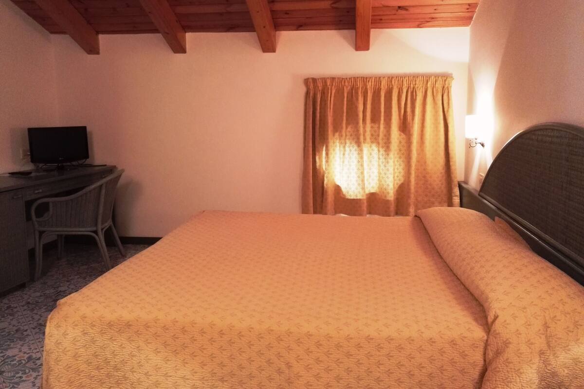 A bedroom with a bed, a desk with a computer, and a window with curtains.