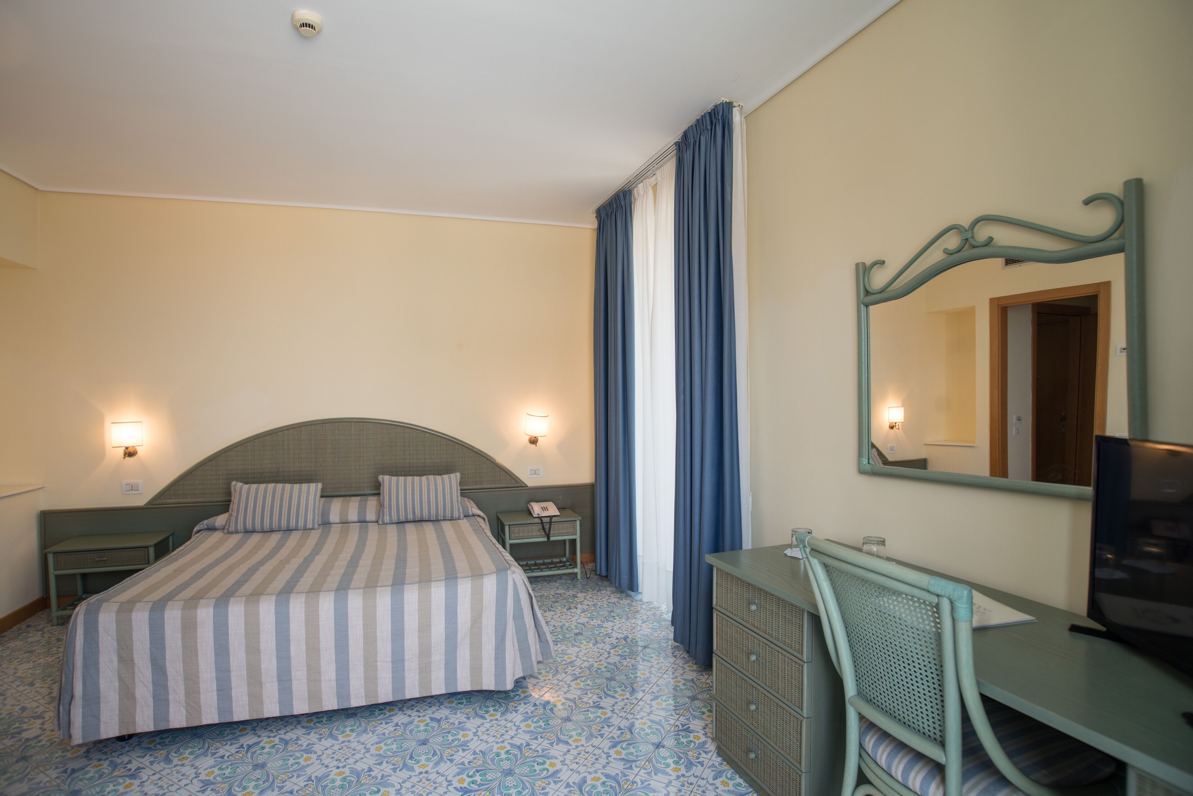 Une chambre d’hôtel équipée d’un lit, de tables de chevet, d’un bureau, d’une chaise, d’un miroir et d’une télévision.