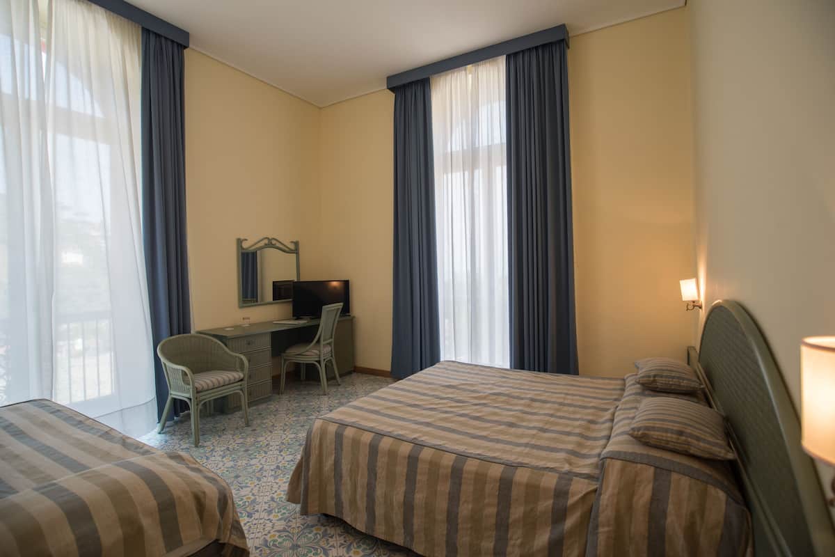 A hotel room with two beds, a desk, a chair, and a television.