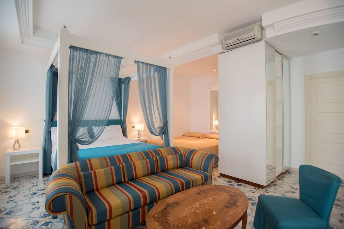 A hotel room with a bed, a striped sofa, a round wooden coffee table, and a blue armchair.