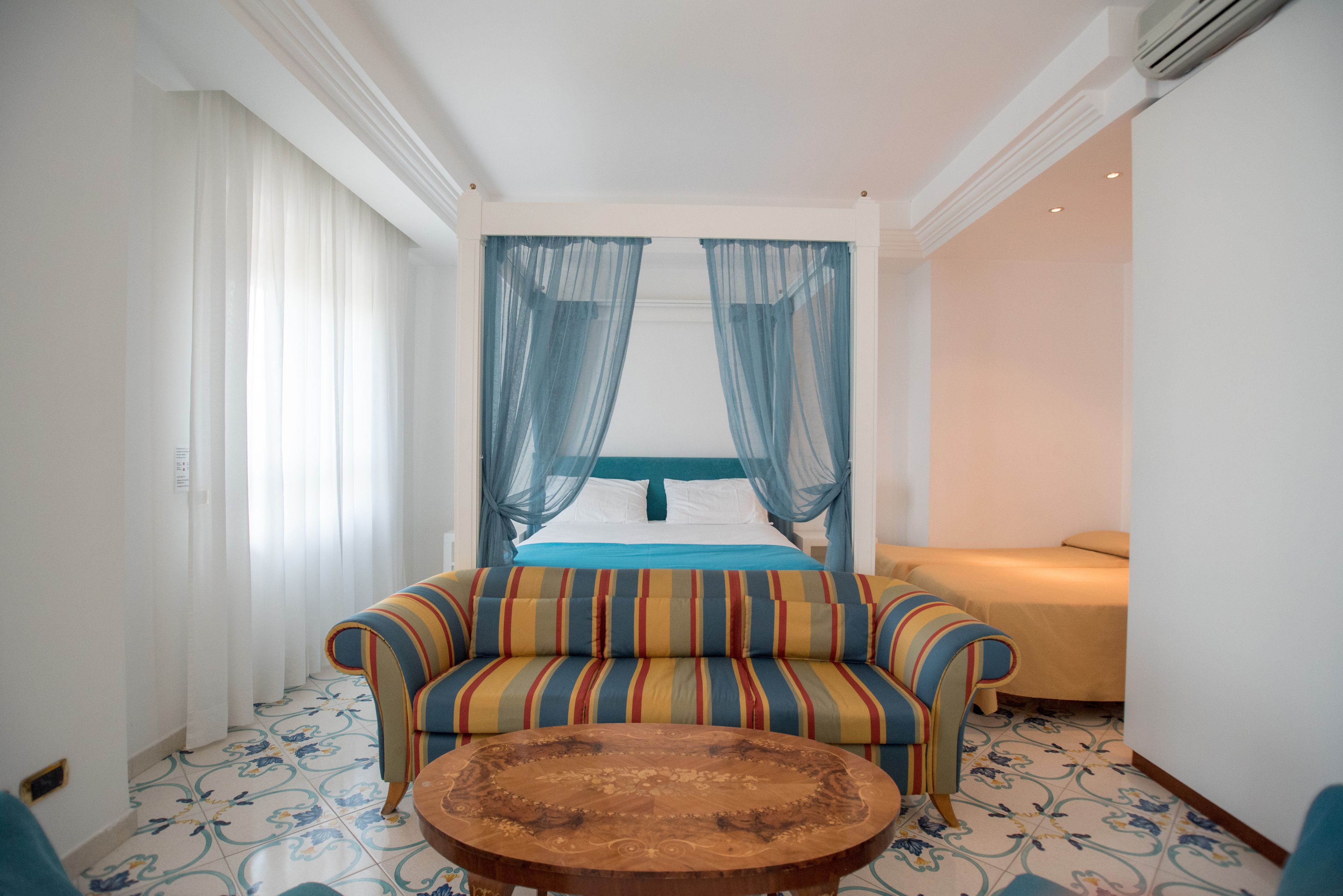 Une chambre d’hôtel avec un lit, un canapé, une petite table et une fenêtre avec des rideaux légers.
