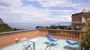 Una terraza en la azotea con una mesa y sillas, vistas al mar y un edificio con balcones.