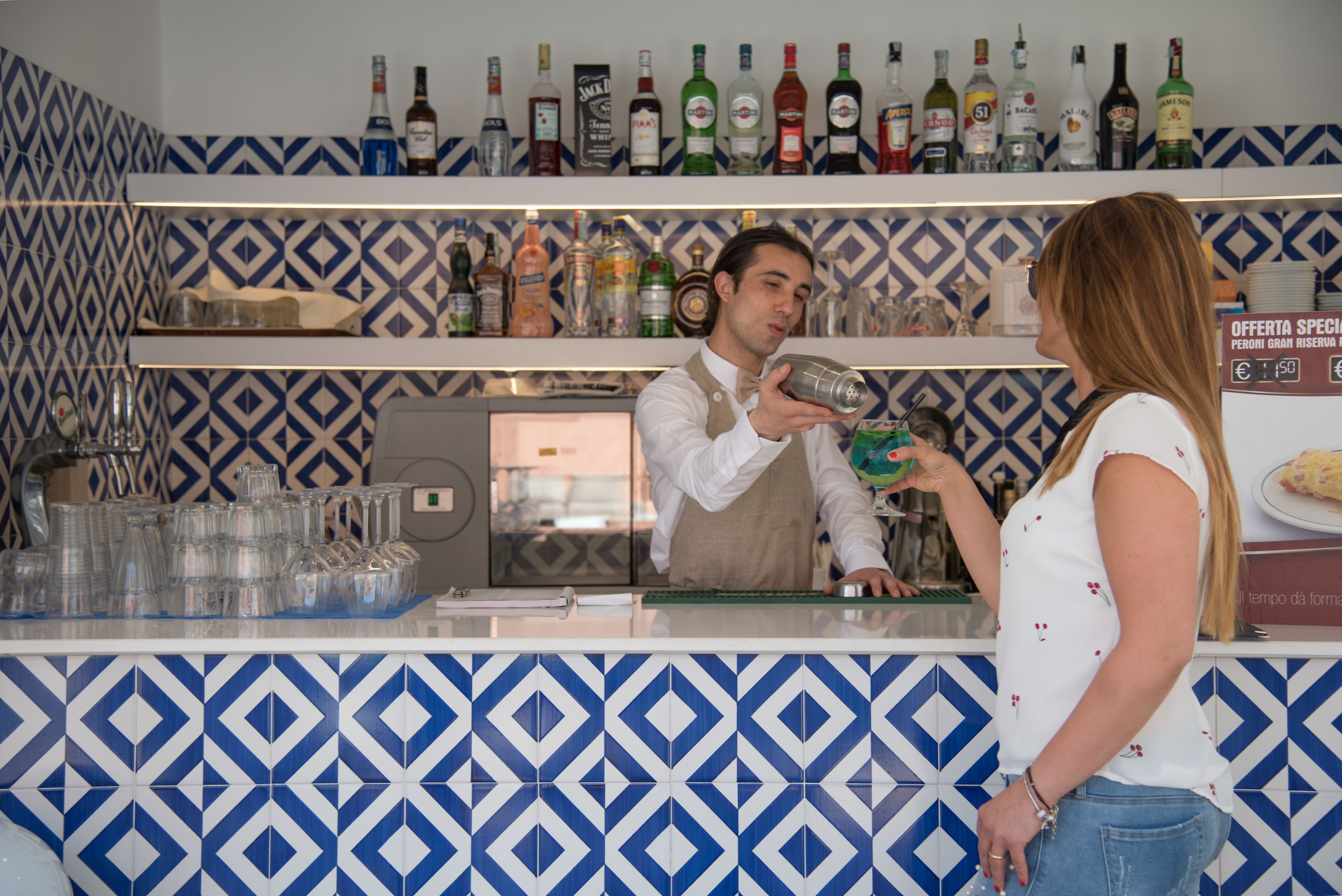 Una zona de bar con un salpicadero de azulejos estampados y estanterías llenas de diferentes botellas de licor.