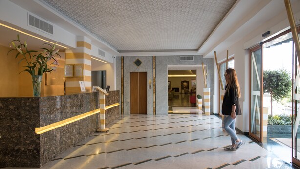 Zona de recepción de hotel con un mostrador de mármol, un jarrón de flores y un mostrador de registro.