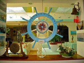 A room with a large ship's wheel as a centerpiece, decorated with various maritime-themed items. - Marconi (Cattolica)