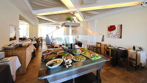A buffet setup with various dishes, a central serving area, and a dining area with tables and chairs. - Hotel Thea (Gabicce Mare)